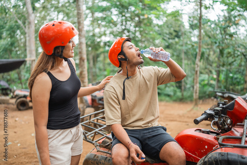 young asian women looking at the asian man that drinking mineral water and sitting on atv at tracking area