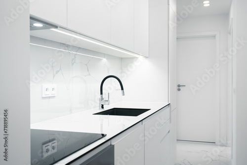 A Modern, bright kitchen with white cabinets, marble countertops, and a sleek sink under minimalist lighting.