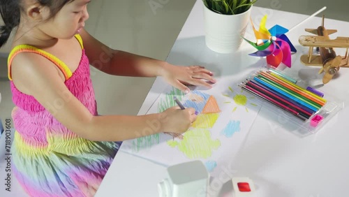 Happy child little girl colorful drawing landscape my home dream on paper, Asian cute kid preschooler sit on table smile she draw country house picture with pencil at home to learning arts homework
