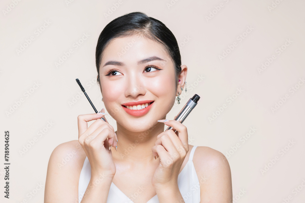 Beautiful asian young woman holding mascara and smiling on purple studio background, Beautiful asian young woman holding mascara and smiling on purple studio background,