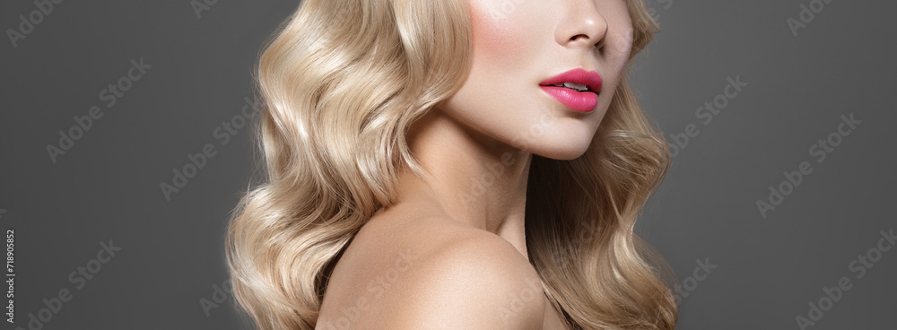 Fototapeta premium Elegant model portrait. Blonde haired Woman with blue eyes and Healthy Long Shiny Wavy hairtyle. Volume shampoo. Blond Curly permed Hair and bright makeup. Beauty salon and haircare concept.