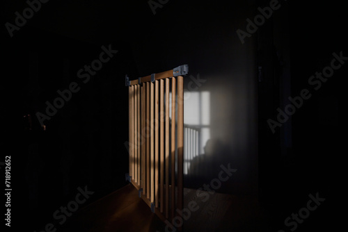 A morning scene featuring a safety baby gate open near a staircase, bathed in sunlight, with a whasto on the adjacent wall photo