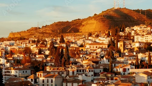 The Albaicin, also known as Albayzin, quarter of Granada, Andalucia, Spain, is bathed in sunset hues, casting a glow over the maze of houses and cypress trees photo