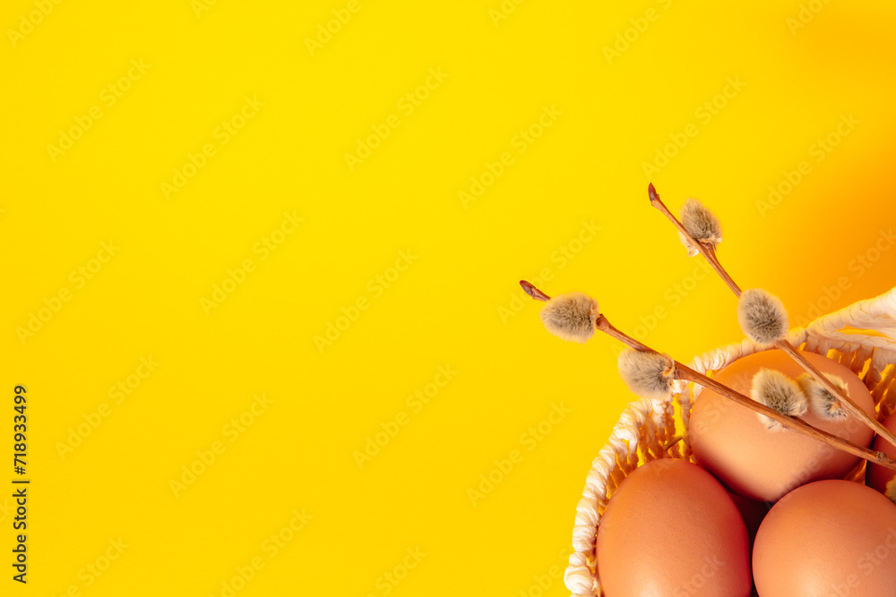 Easter holiday card with basket full of eggs on yellow background decorated with a pussy willow twigs. Copy space. Empty text place. Springtime mockup design. Healthy food. Farm production. Close-up
