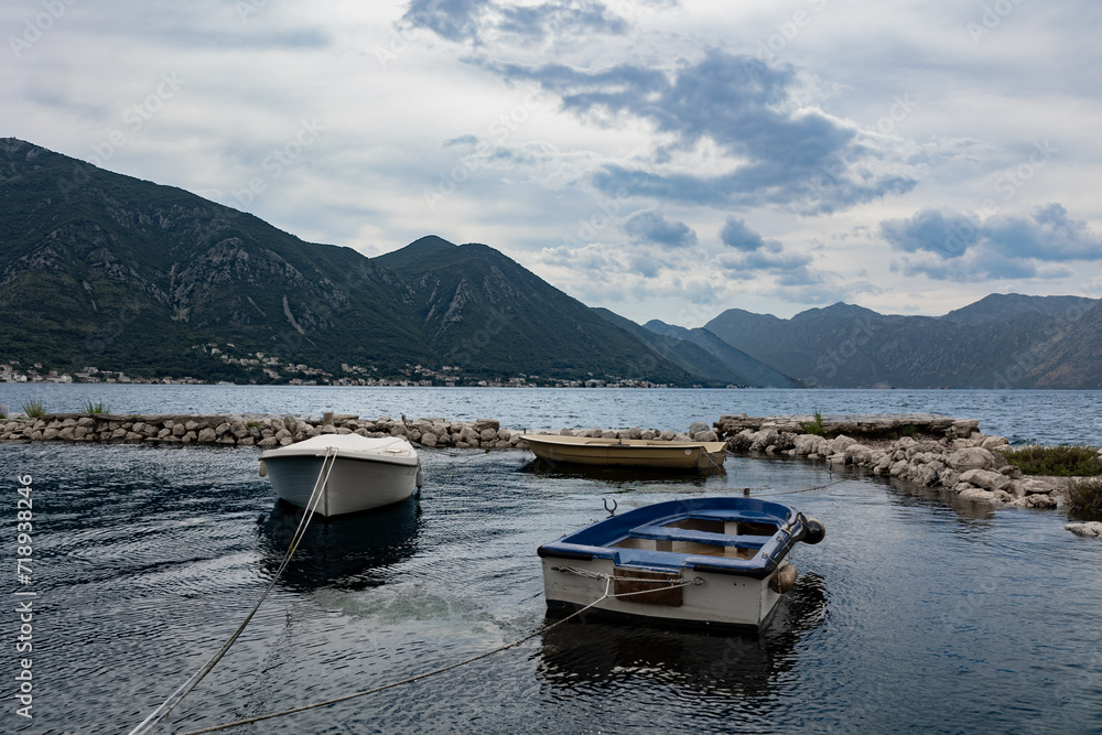 Kotor, Montenegro - 06 17 2023: Two fishing boats docked in Kotor bay facing the mountains underneath a cloudy sky