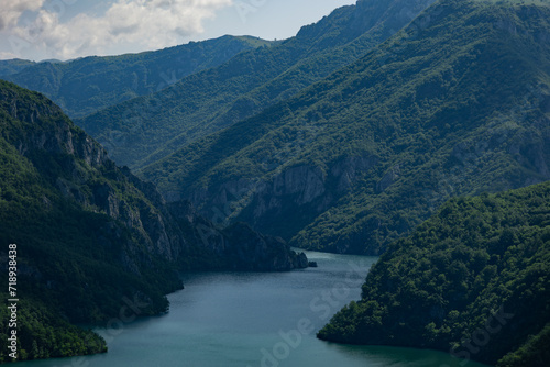 Panoramic view of the bluish water of the Piva river in Montenegro, cutting through the green mountains under the cloudy skies