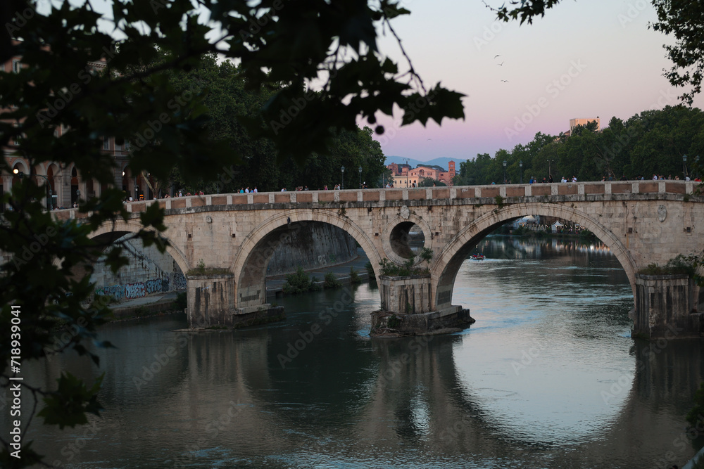 Rome, Italy - 06 26 2023: Ponte Sisto bridge spanning the river Tiber at dusk. Tourists gathered on it watching the pretty scene