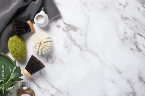 Cleaning products style border design with gray towels, brushes and sponges with green leaves on marble background. Hygiene and housework on surface with space to place text.