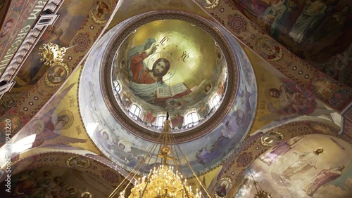 The majestic dome of an Orthodox church, adorned with the Christ Pantocrator fresco, surrounded by ornate murals and a hanging chandelier.