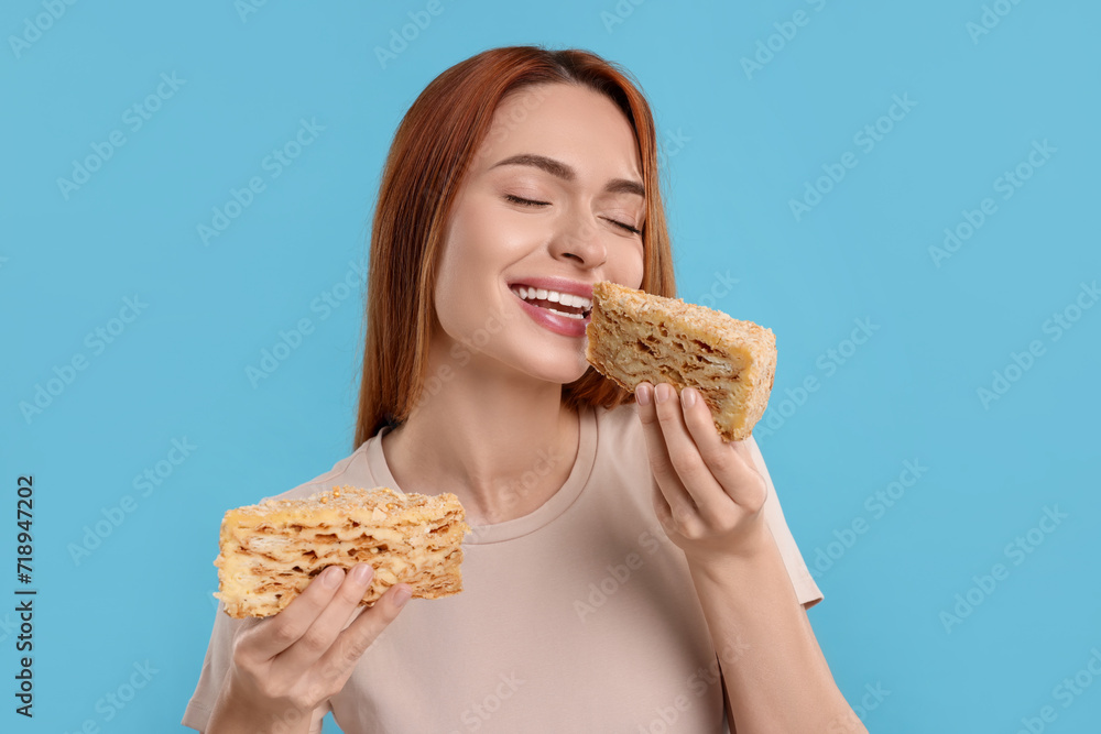 Young woman eating pieces of tasty cake on light blue background