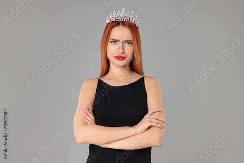 Emotional young woman with tiara in dress on light grey background