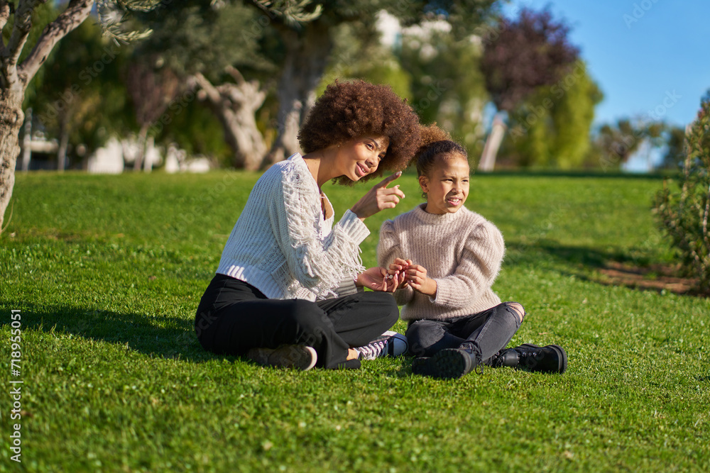two curly-haired latina sisters sitting on the grass watch with some admiration. family time two curly-haired latina sisters sitting on the grass watch with some admiration. family time