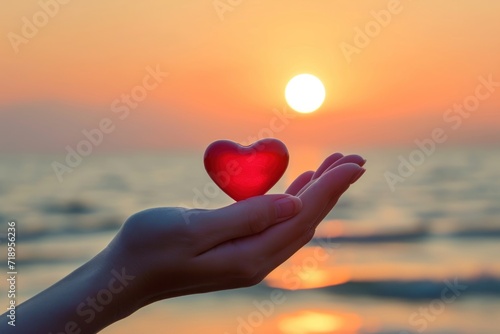 Woman hand holding red heart at sunset 