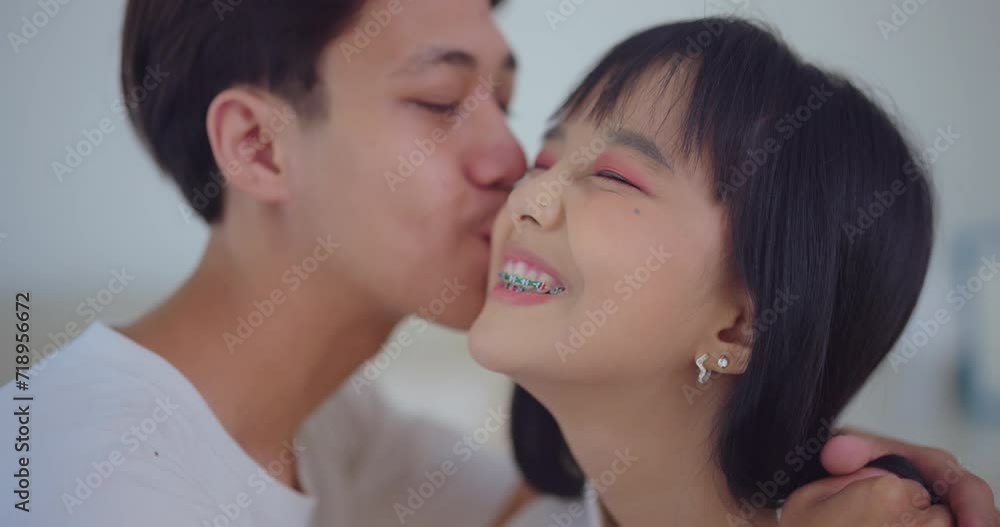 Young Asian couple shares a tender kiss in the cozy embrace of their living room, reveling in the joy of this intimate moment together. Young Asian couple shares a tender kiss in the cozy embrace of their living room, reveling in the joy of this intimate moment together.