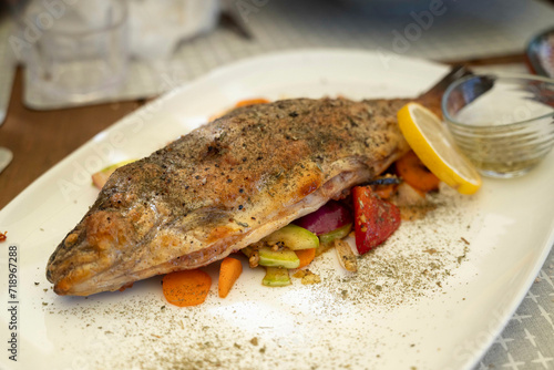 Baked trout fish, served on a white plate with vegetables and fresh lemon and herbs