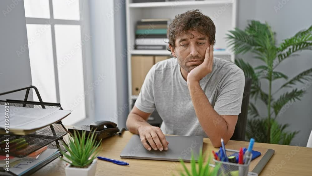 Pensive man with beard in casual clothing at modern workplace contemplating while sitting with arms crossed by the laptop Pensive man with beard in casual clothing at modern workplace contemplating while sitting with arms crossed by the laptop