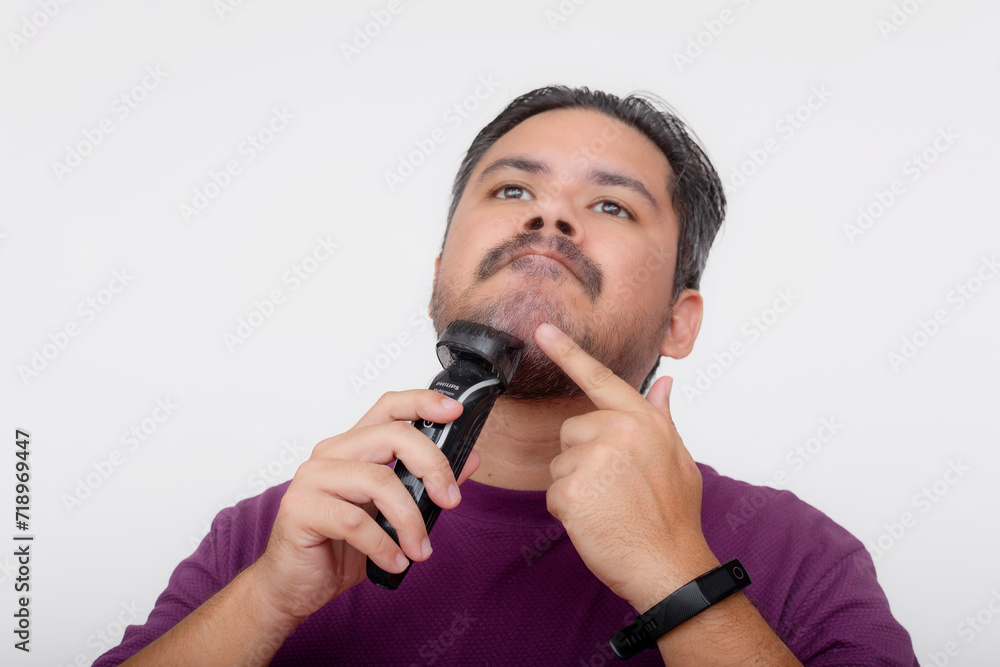 A middle aged man using a cordless trimmer to shape and trim his beard. Facial care and grooming. Looking at camera, isolated on a white background. A middle aged man using a cordless trimmer to shape and trim his beard. Facial care and grooming. Looking at camera, isolated on a white background.