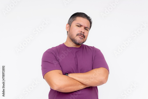 Portrait of a doubtful adult man with arms crossed, wearing a purple t-shirt, isolated on a white background.