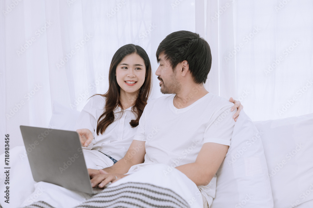 Happy asian man and woman using laptop sitting relaxed on a bed at home enjoy, Happy lover hug each other and smiling on the bed, Male and female couple concept. Happy asian man and woman using laptop sitting relaxed on a bed at home enjoy, Happy lover hug each other and smiling on the bed, Male and female couple concept.