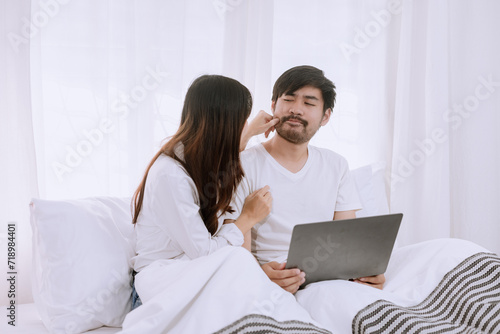 Happy asian man and woman using laptop sitting relaxed on a bed at home enjoy, Happy lover hug each other and smiling on the bed, Male and female couple concept. © SOMKID