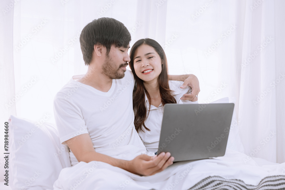 Happy asian man and woman using laptop sitting relaxed on a bed at home enjoy, Happy lover hug each other and smiling on the bed, Male and female couple concept. Happy asian man and woman using laptop sitting relaxed on a bed at home enjoy, Happy lover hug each other and smiling on the bed, Male and female couple concept.