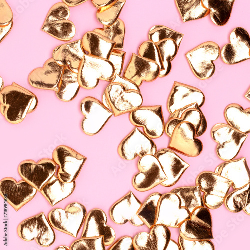 Golden hearts confetti scattered on a pink background. Festive texture.
