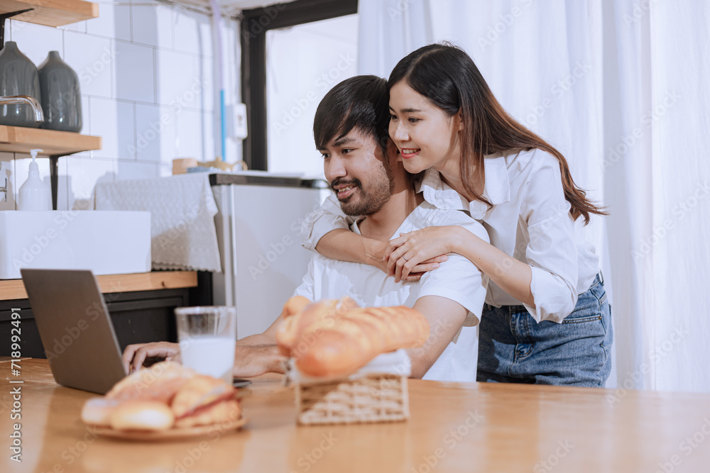 Happy love Asian young man and woman using laptop together in the kitchen relaxing at home. Happy love Asian young man and woman using laptop together in the kitchen relaxing at home.
