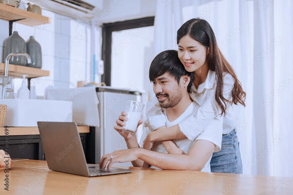 Happy love Asian young man and woman using laptop together in the kitchen relaxing at home. Happy love Asian young man and woman using laptop together in the kitchen relaxing at home.