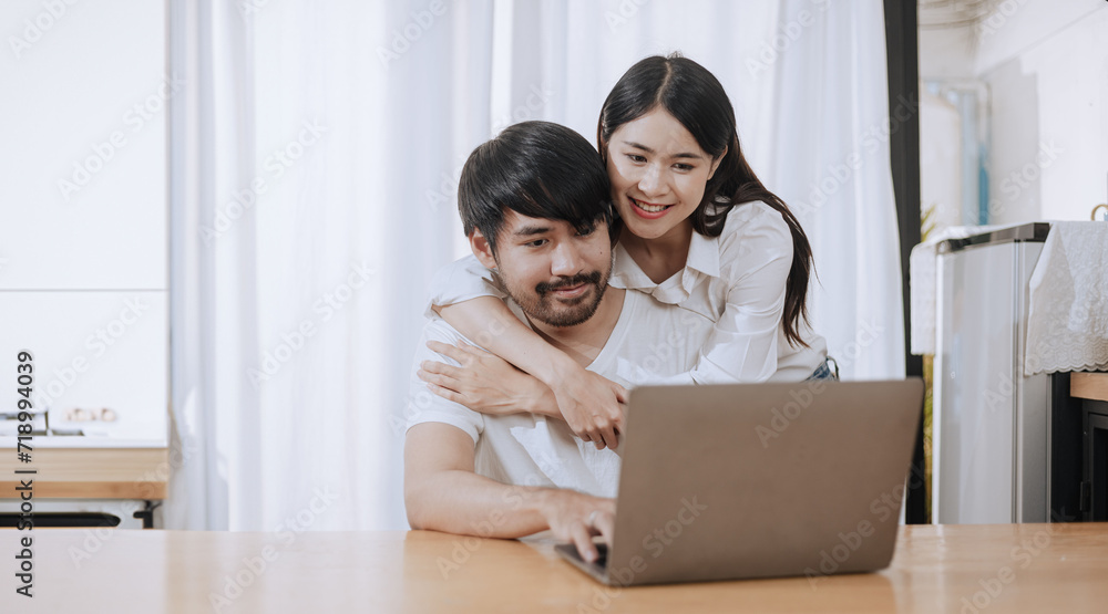 Happy love Asian young man and woman using laptop together in the kitchen relaxing at home. Happy love Asian young man and woman using laptop together in the kitchen relaxing at home.