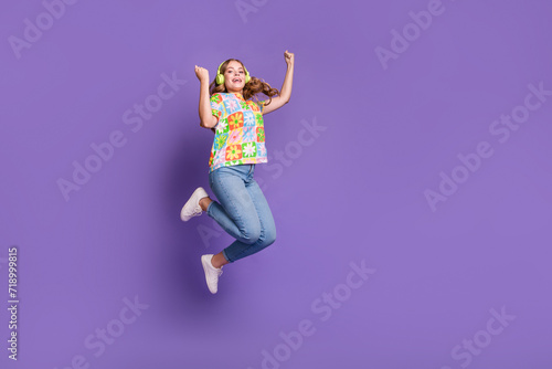 Full size photo of satisfied girl dressed print t-shirt jeans jumping in headphones win lottery isolated on violet color background