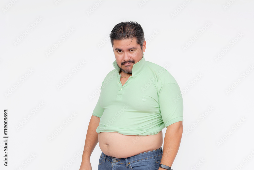 An overweight man looks annoyed after his old shirt barely fits, his belly sticking out. A consequence of gaining too much weight. Isolated on a white background. An overweight man looks annoyed after his old shirt barely fits, his belly sticking out. A consequence of gaining too much weight. Isolated on a white background.