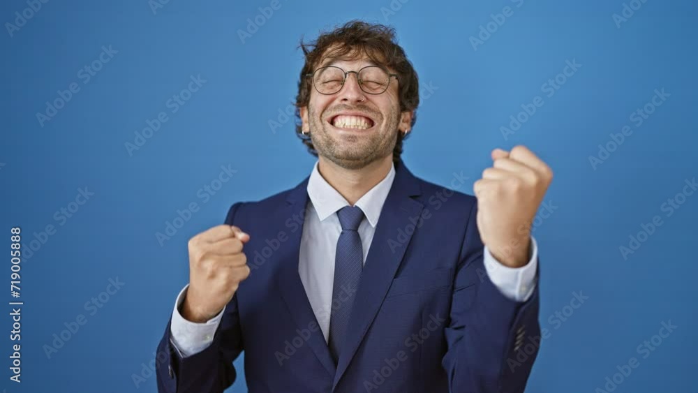 Joyful young man in business suit, hispanic and blond, celebrates triumph arms raised. epic win, beaming with success! isolated on a blue background. Joyful young man in business suit, hispanic and blond, celebrates triumph arms raised. epic win, beaming with success! isolated on a blue background.