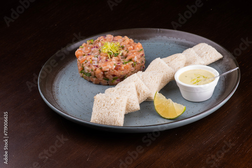 raw salmon tartare with toast sauce and lemon on rustic ceramic plate from an angle