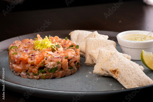 raw salmon tartare with toast sauce and lemon on rustic ceramic plate close-up