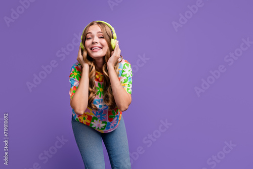 Portrait of satisfied positive cute girl with curly hairdo touching headphones listen playlist isolated on violet color background © deagreez