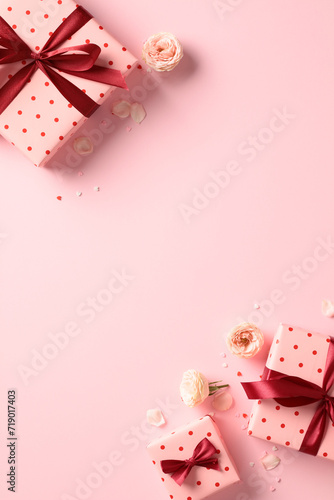 Top view photo of Valentines Day gifts with red ribbon bow, roses buds on pastel pink vertical background. Flat lay.