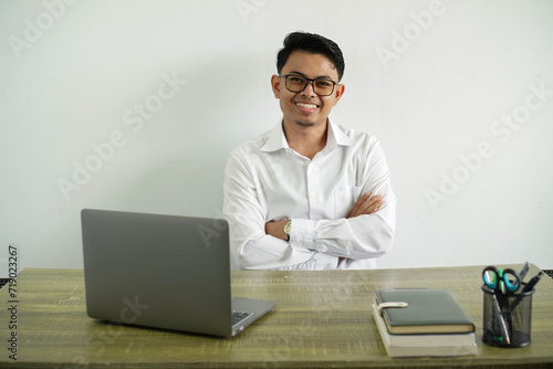 smiling young asian businessman in a workplace crossing his arms with looking camera, wearing white shirt with glasses isolated