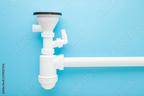 Assembled white new plastic parts for sink drain siphon on light blue table background. Pastel color. Closeup. Top down view. photo