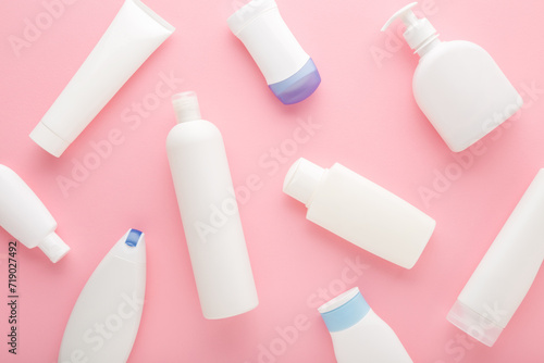 Different white plastic cosmetic bottles on light pink table background. Pastel color. Care about clean and soft body skin. Daily beauty product pattern. Closeup. Top down view.