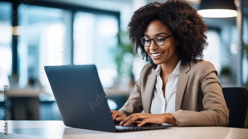 midst the hustle and bustle of the office, a happy African American businesswoman engages with her laptop