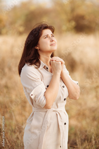 portrait of young woman praying on nature, girl thanks God with her hands folded under chin, concept of religion © fantom_rd