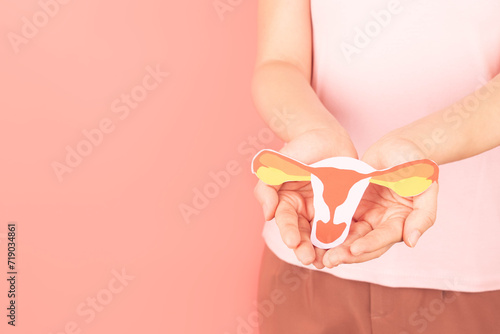 Female reproductive health concept. Woman hand holding uterus shape made from paper on pink background. Awareness of uterus illness such as endometriosis, PCOS, STDs, HPV or gynecologic cancer. photo