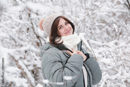 happy young woman in knitted hat and warm scarf among trees covered with snow, girl walking on winter forest enjoying beautiful nature