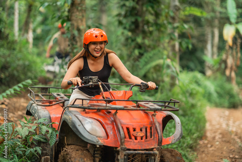 happy asian woman riding atv through the atv track leaving her partner behind
