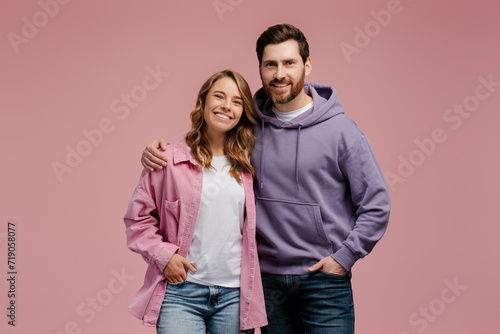 Portrait of attractive smiling couple hugging isolated on pink background. Happy bearded man and beautiful woman wearing stylish casual clothing looking at camera in studio photo