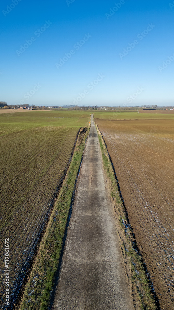 This image presents a vertical, linear perspective of a country road cutting through the winter fields. On either side, the contrast between the harvested field and the one awaiting cultivation is