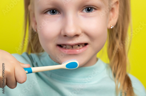 The face of a smiling seven-year-old girl on a yellow background with a toothbrush in her hands. Concept of teeth care and cleaning. Oral hygiene in dentistry, close-up