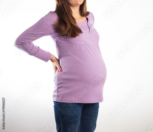 A pregnant girl in a purple sweater on a white background holds on to her back with back pain. The concept of chronic diseases in pregnant women osteochondrosis and intervertebral hernia. photo