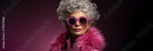 Beautiful adult elderly elegant white platinum blonde woman with pink sunglasses, earrings and magenta leather jacket on purple background. Age. Gray hair. Horizontal banner. March 8
