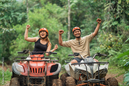 young asian couple clenched their hand and yelling happily while riding atv through the track inside amusement park photo